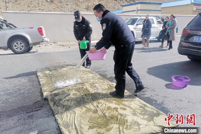 圖為日喀則噶拉邊境檢查民警利用消毒水沁濕的棉被對(duì)過往車輛輪胎消毒。　李強(qiáng) 攝
